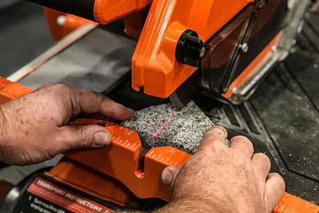 Close-up of hands positioning a granite tile under a laser-guided dry saw for precise cutting.