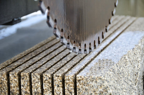 Close-up of an industrial diamond saw blade cutting through thick granite slabs.